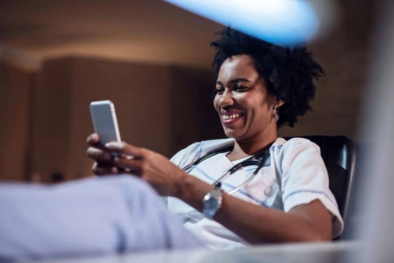 Smiling female doctor using smart phone and typing a message during her break. Smiling female doctor using smart phone and typing a message during her break.