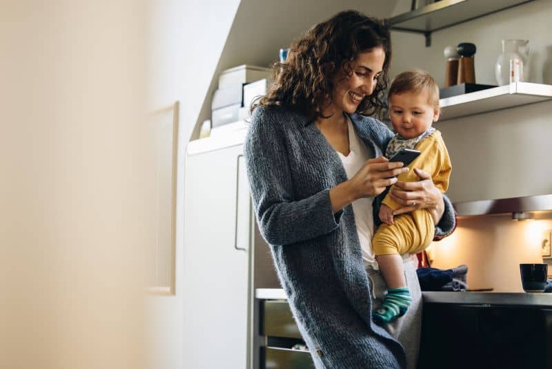Smiling woman using mobile phone while carrying baby. Smiling woman using mobile phone while carrying baby.