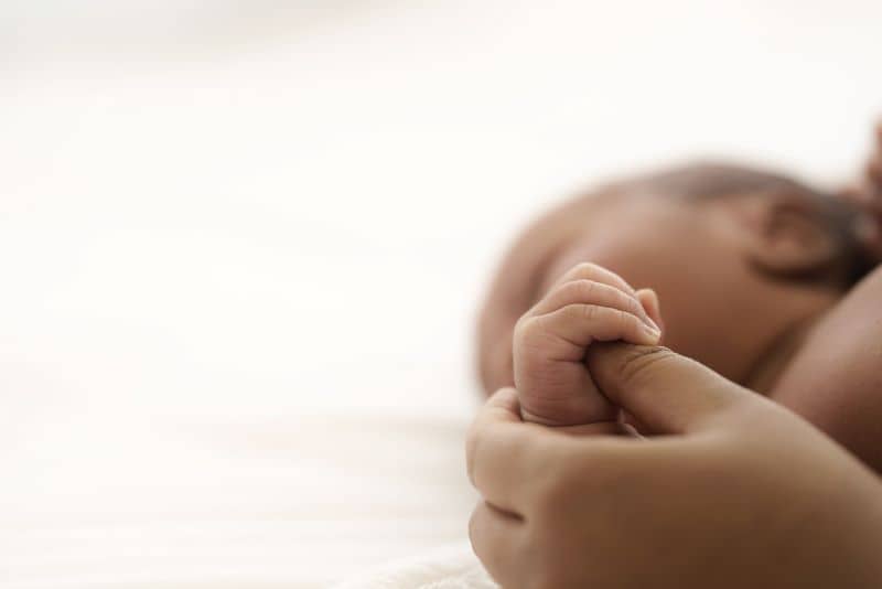 Baby lying on bed while mother hands pull baby up. Baby lying on bed while mother hands pull baby up.