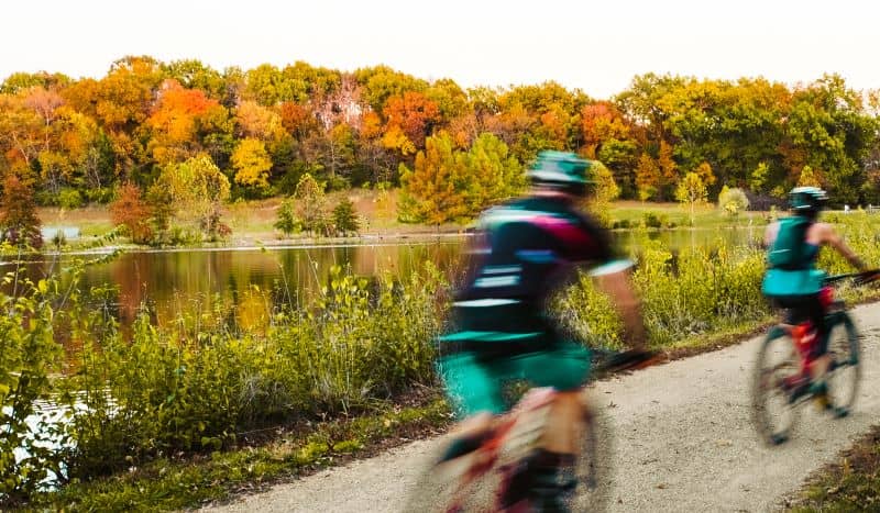 Blurry view of two bicyclist riding by Midwestern lake in fall. Blurry view of two bicyclist riding by Midwestern lake in fall.