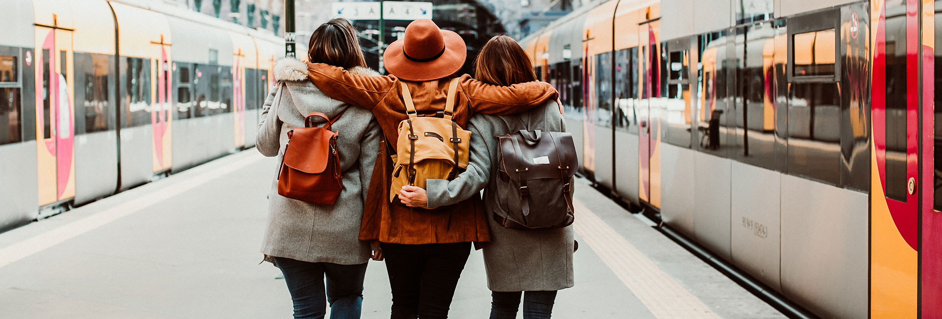 Three female nursing wearing backpacks and embracing while standing near a train station.