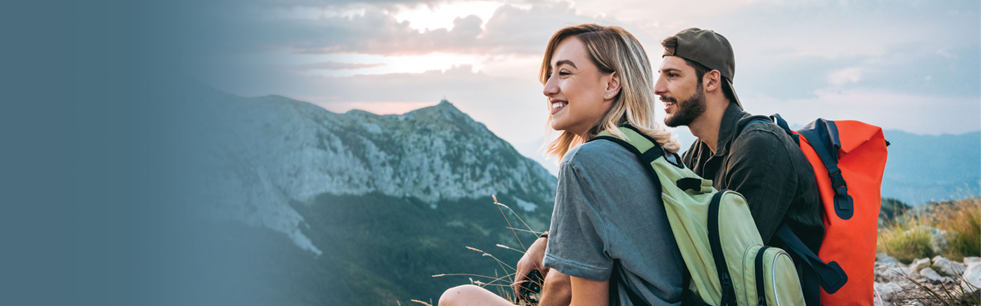 Two, happy travel nurse hikers sitting on a mountaintop wearing backpacks.